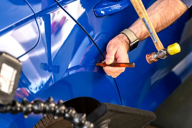 Ein Mitarbeiter entfernt eine Beule an einem blauen Auto. 