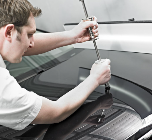Ein Experte für Unfallinstandsetzung behebt Dellen auf der Motorhaube eines schwarzen Autos mittels modernster Technik. 