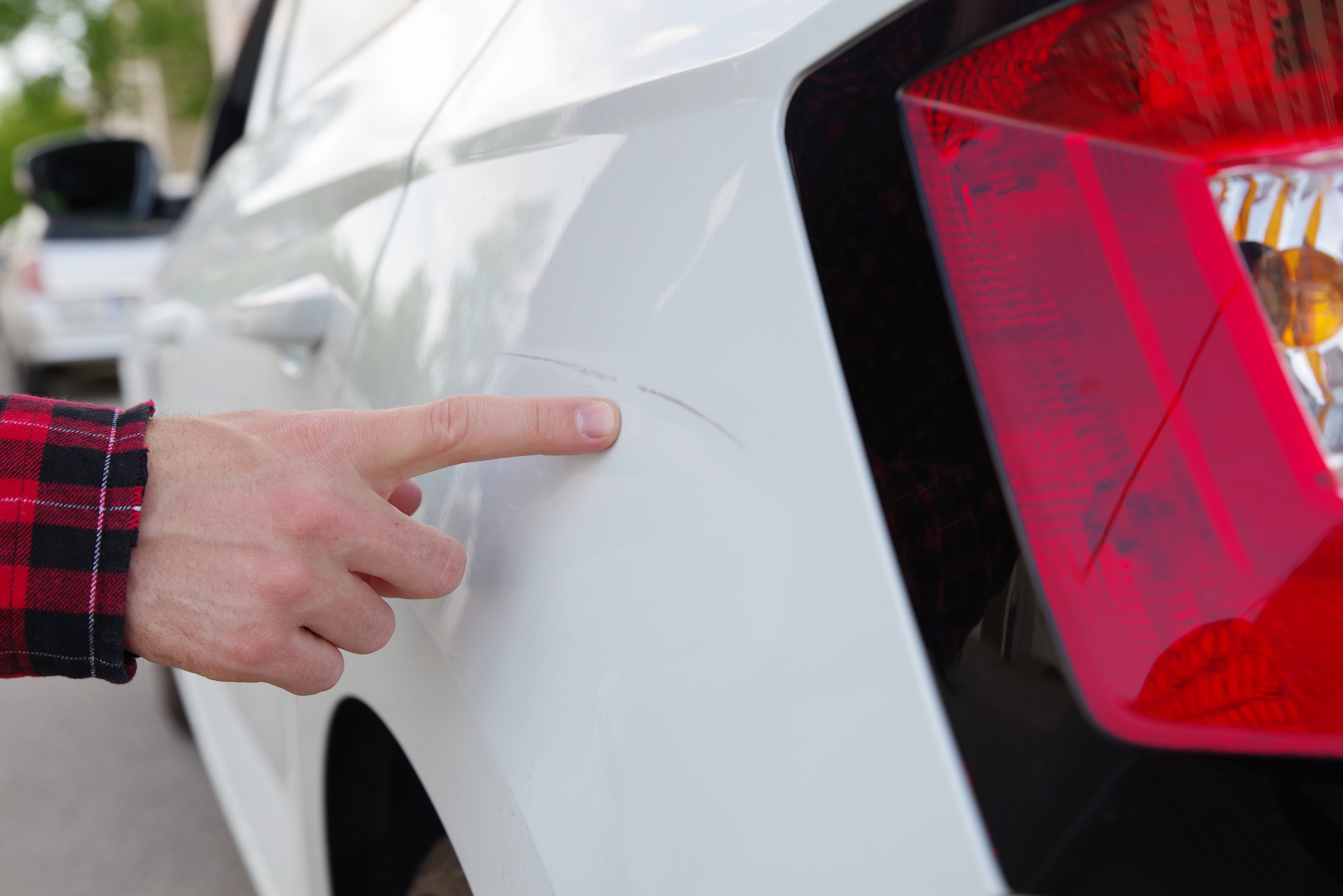 Eine Hand zeigt einen Kratzer auf einem weißen Auto. Der Kratzer kann mithilfe der Smart Repair in Bergisch Gladbach entfernt werden.
